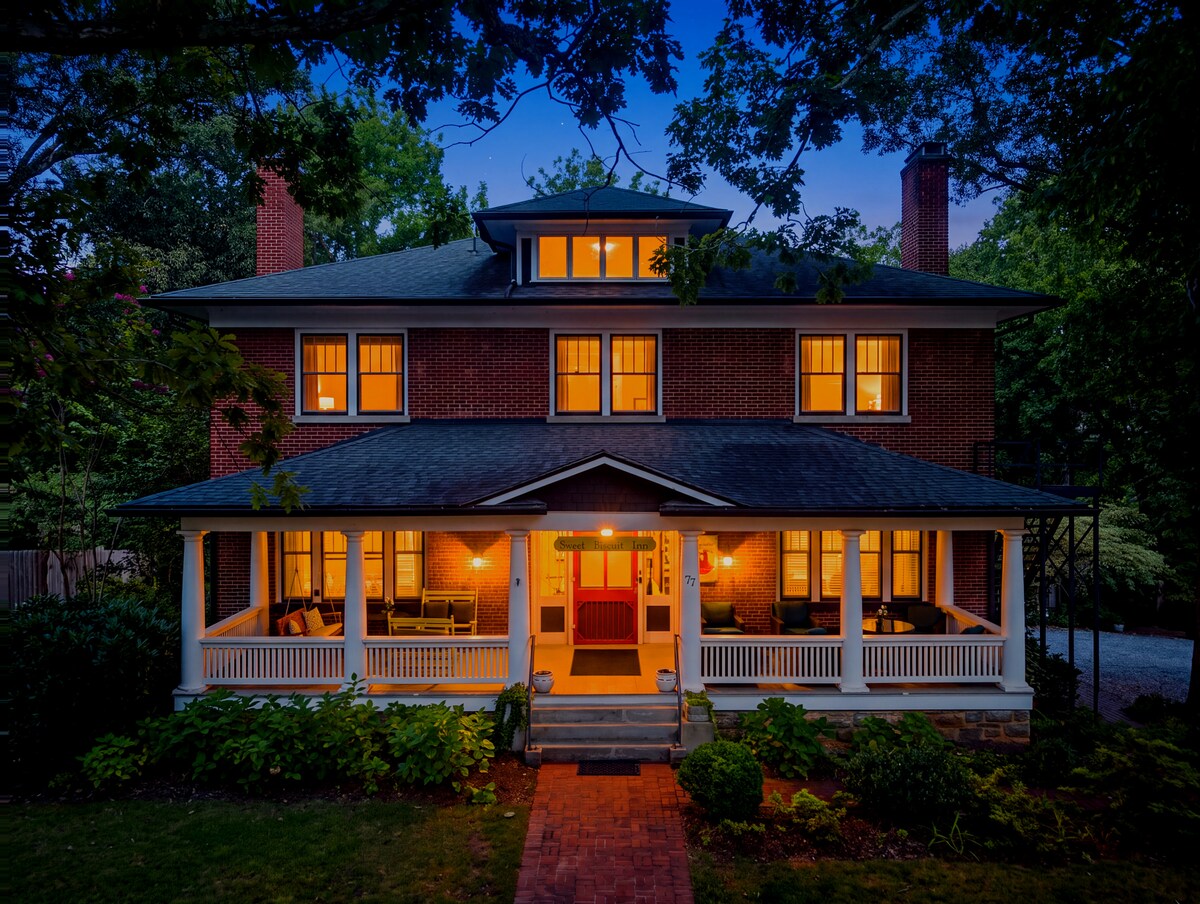 A two-story brick house with a large porch and a red door at dusk.