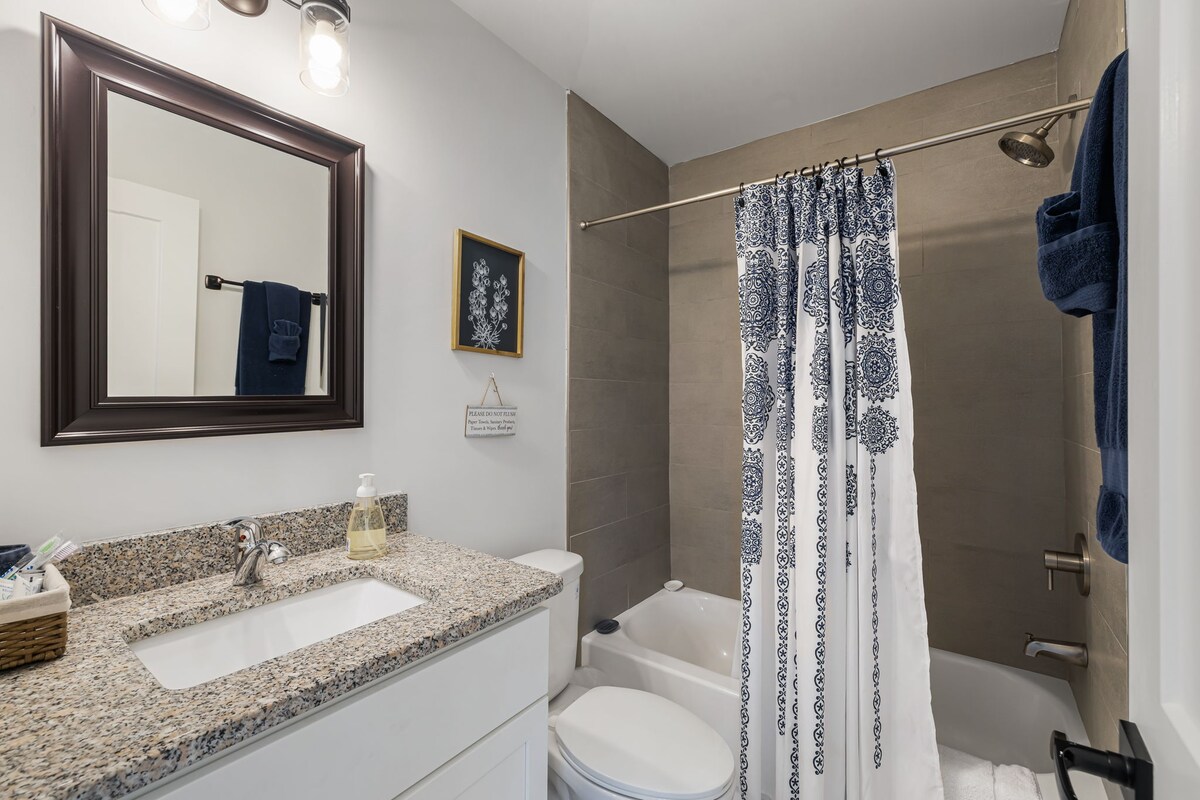 A clean bathroom with a granite countertop, white sink, toilet, and shower with a blue and white shower curtain.