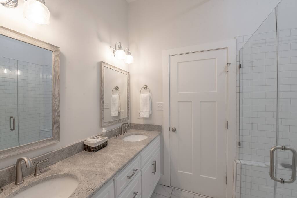 A clean and modern bathroom with a double vanity, a large mirror, and a shower