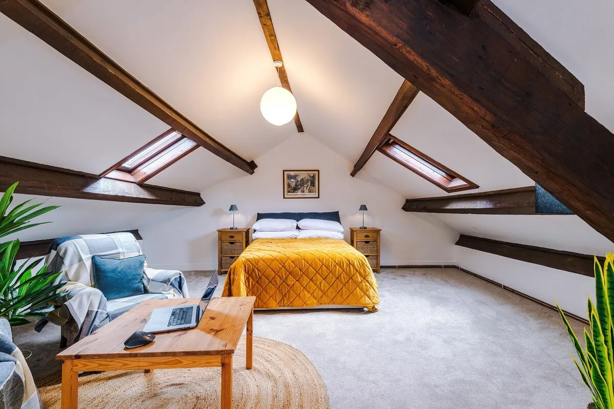 Attic bedroom under oak beams, with a mustard throw and a sofa