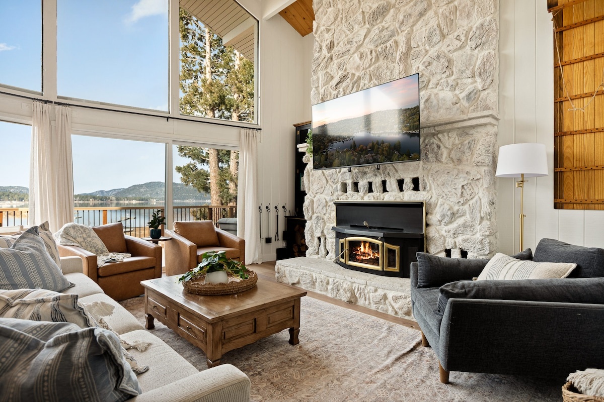 Lakefront cabin living room with tall stone fireplace, vaulted ceilings, and Big Bear Lake views