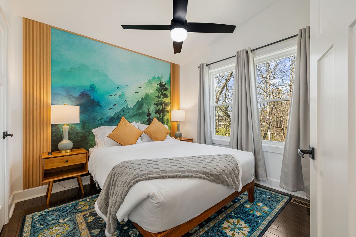 A wide view of a guest room with a bed, nightstands, lamps, and a large piece of artwork on the wall.