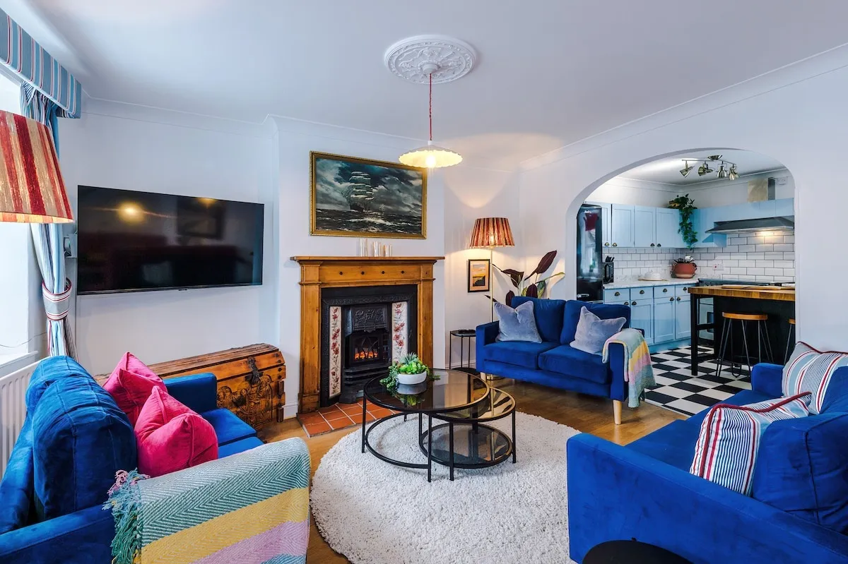 Lounge with two navy sofas around a round rug, the kitchen through the arch