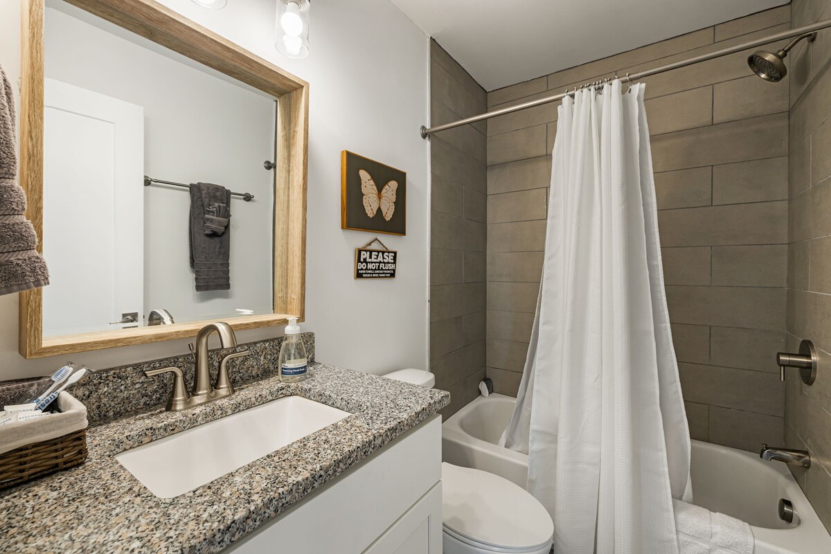 A clean bathroom with a granite countertop, shower curtain, bathtub, toilet, and mirror.