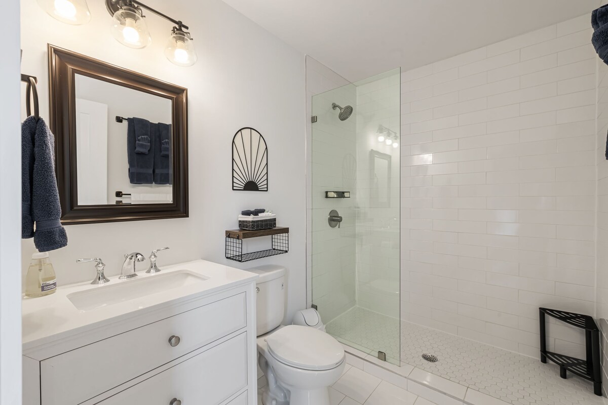 A clean and modern bathroom with a glass-enclosed shower, white tiles, and a single sink vanity.