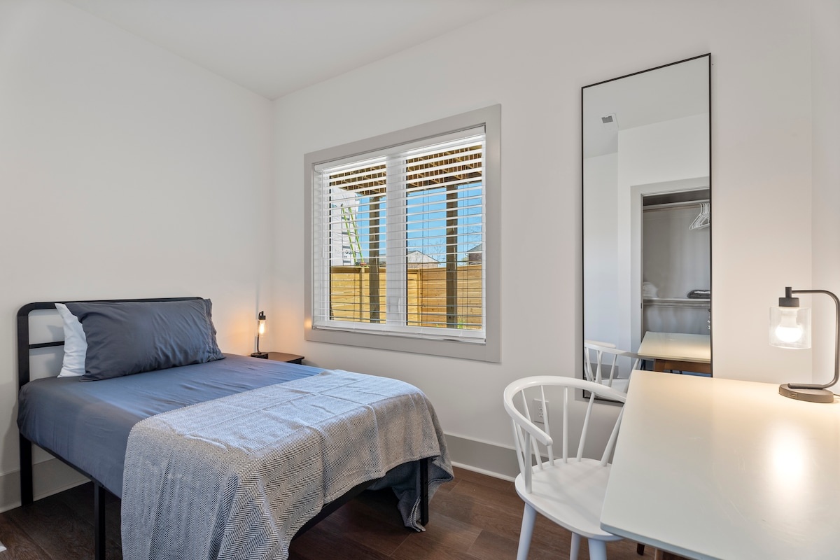 A small hotel room with a bed, desk, mirror, and window.
